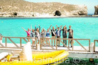 A group of students waving next to a boat at the Blue Lagoon, Comino