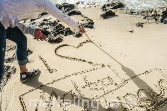 A student writing I 'heart' Maltalingua in the sand