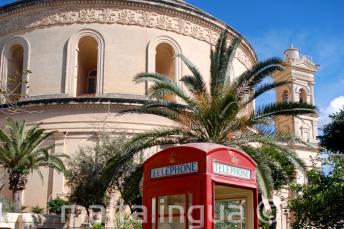 A red telephone box in front of the Mosta Rotunda