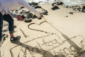 A student writing I 'heart' Maltalingua in the sand