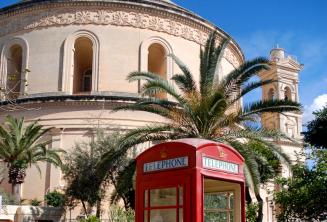 A red telephone box in front of the Mosta Rotunda